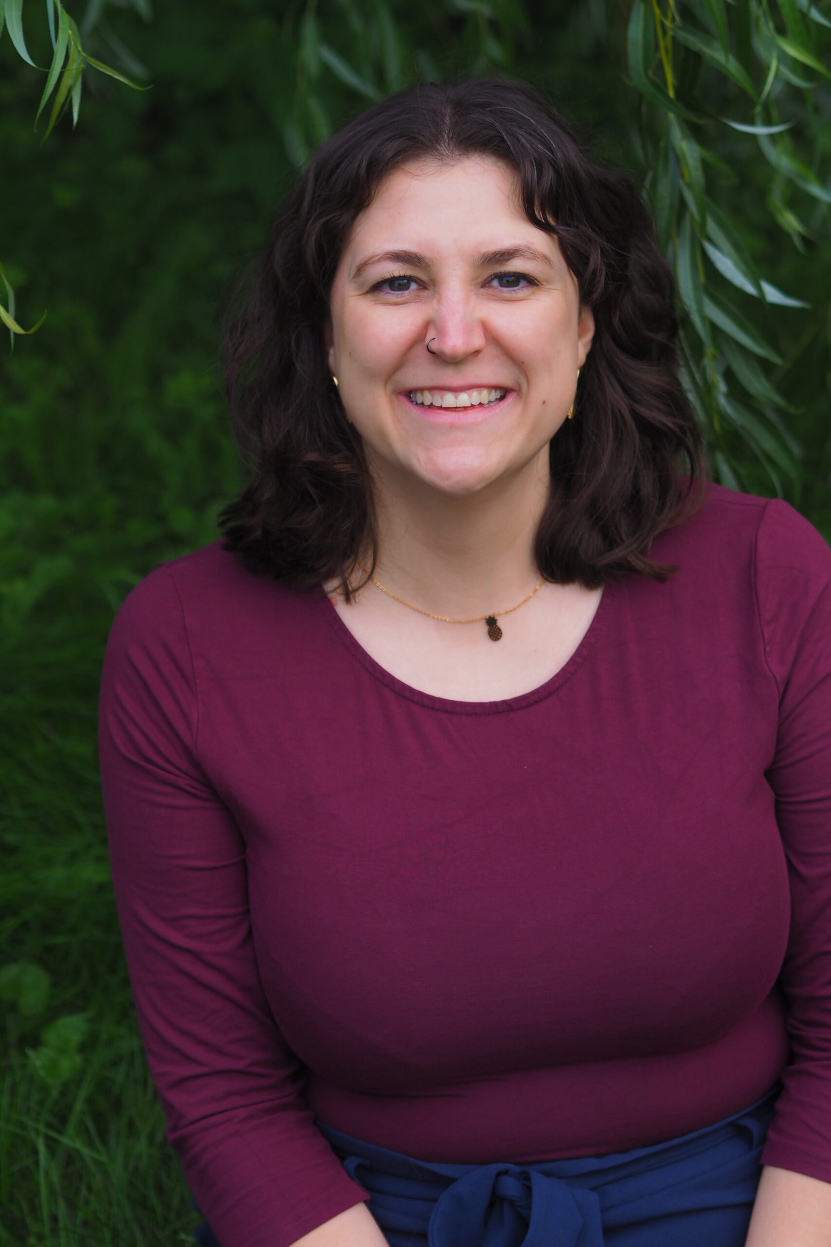 Mimi steht vor einem grünen Busch und lächelt leicht in die Kamera,